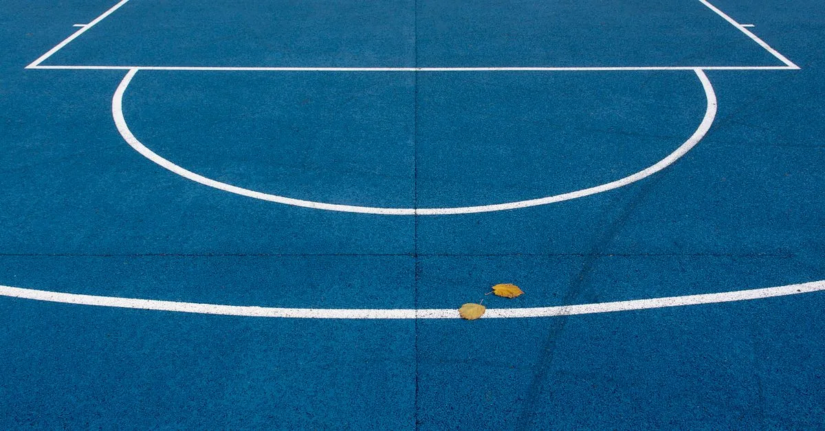An empty blue basketball court with white lines and leaves on the surface.