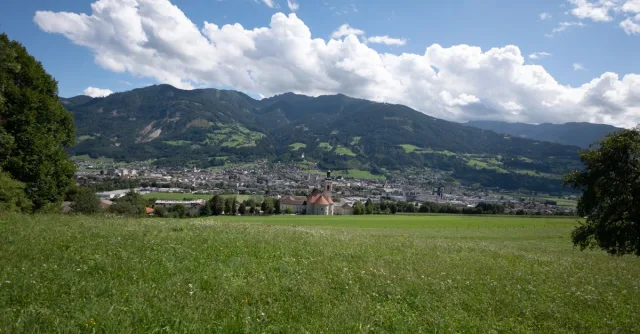 Lush green fields and majestic mountains under a clear sky in Tirol, Austria.