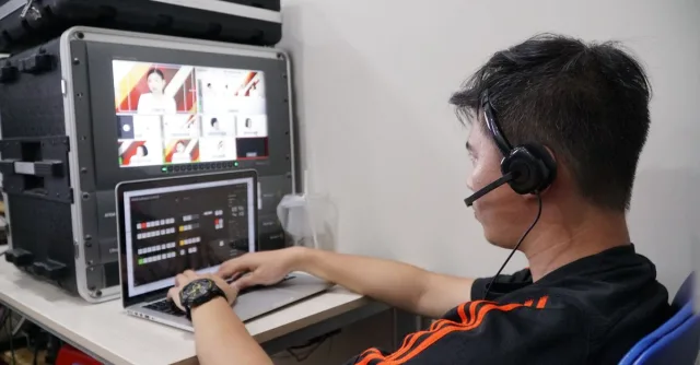 Technician manages multiple video feeds using laptop and monitor in studio setting.