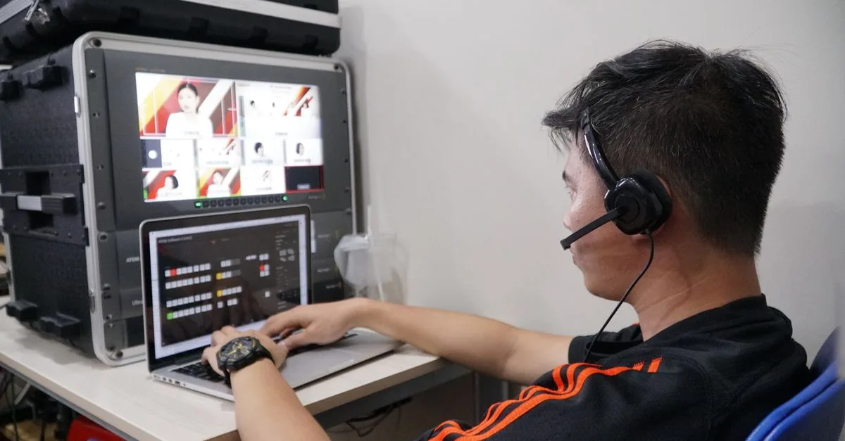 Technician manages multiple video feeds using laptop and monitor in studio setting.