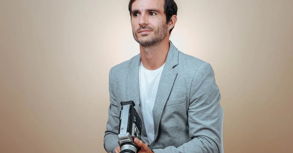 Man sitting with a vintage camera against a beige background in studio lighting.