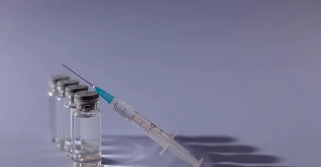 Syringe and vaccine vials arranged on gray surface, symbolizing healthcare and immunization.