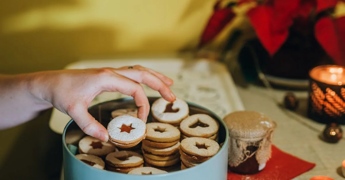 Hand picking delicious star-shaped Christmas cookies from a festive tin, perfect for holiday celebrations.