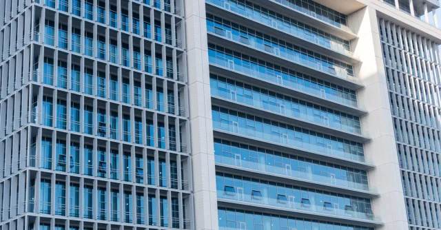 A modern office building with glass facade, featuring urban city architecture and blue sky reflections.