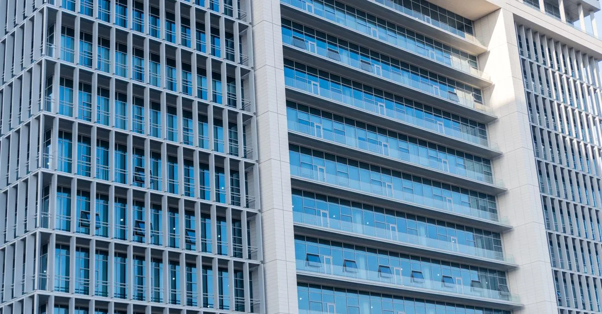 A modern office building with glass facade, featuring urban city architecture and blue sky reflections.