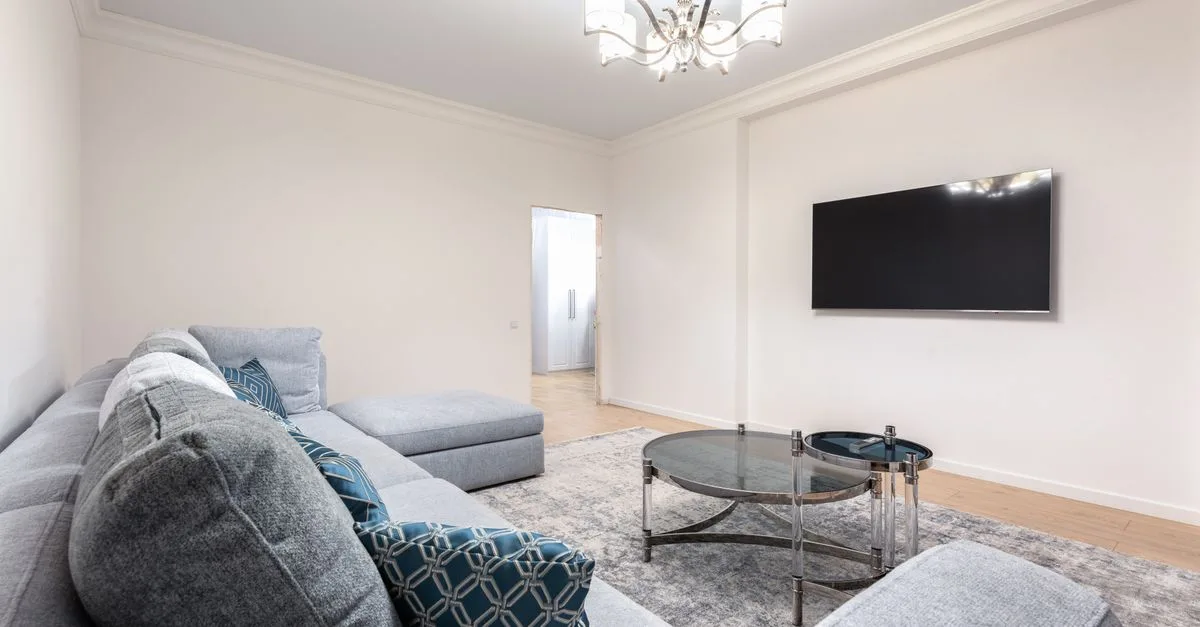 Contemporary room interior with couch and TV with black screen against tables under shiny chandelier in house