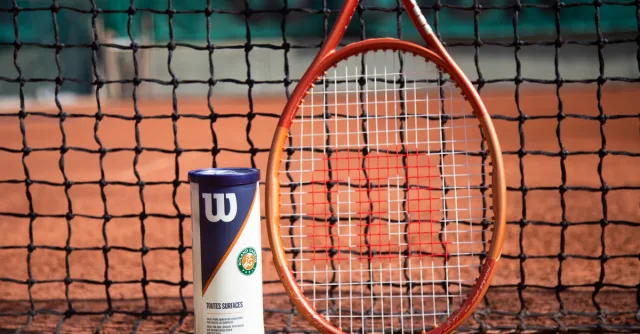 Tennis racket and ball can in front of a net on a clay court, showcasing sports equipment.
