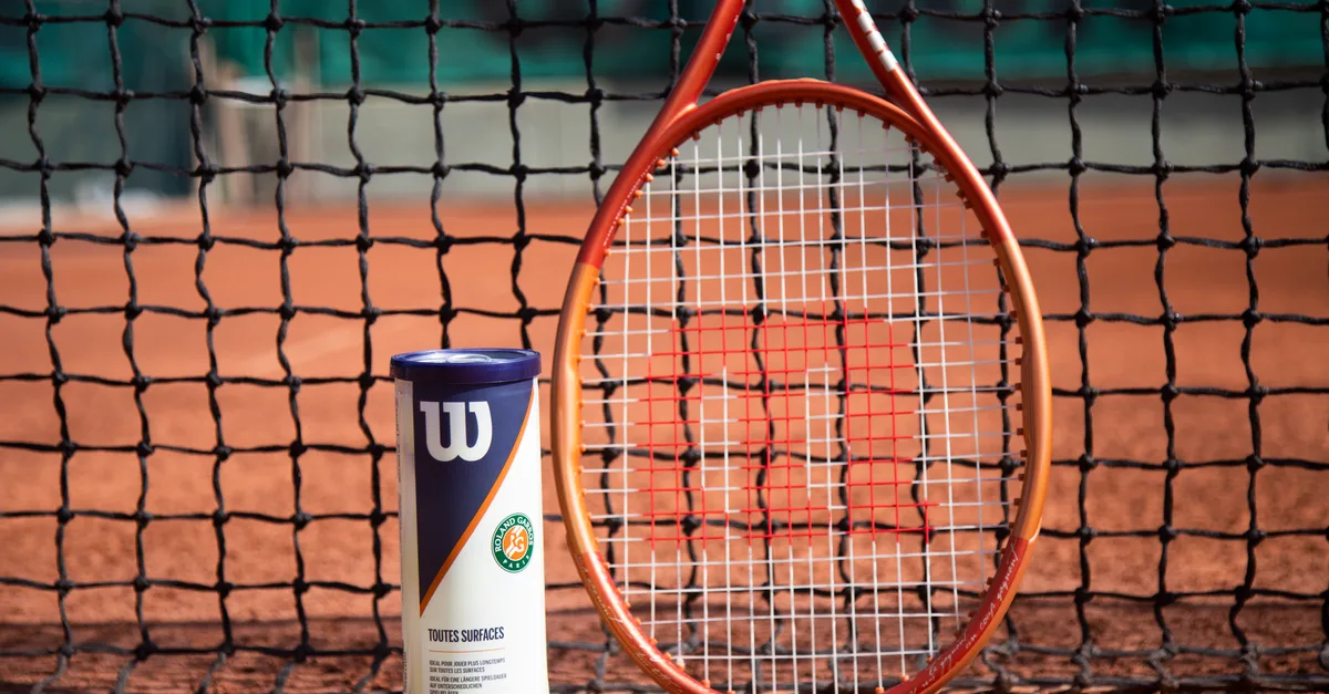 Tennis racket and ball can in front of a net on a clay court, showcasing sports equipment.