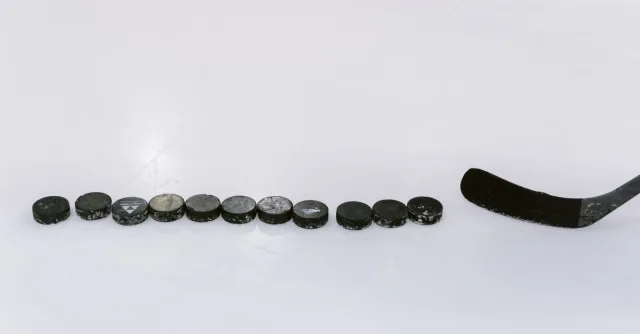 A row of hockey pucks and a stick on an ice rink, perfect for sports content.