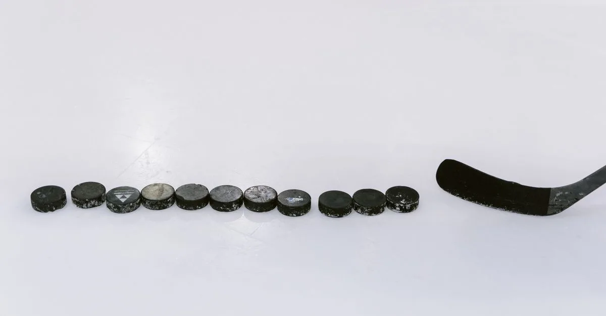 A row of hockey pucks and a stick on an ice rink, perfect for sports content.