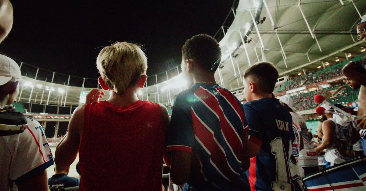 Fans cheer from the stands during a night soccer game in a large stadium, full of energy and excitement.