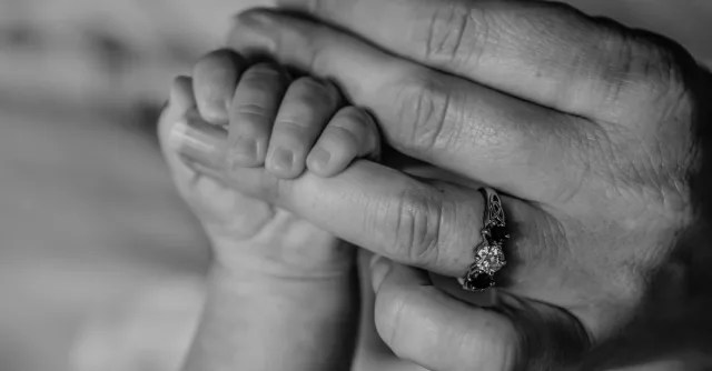 Close-up black and white photo of baby hand holding mother's finger with love.