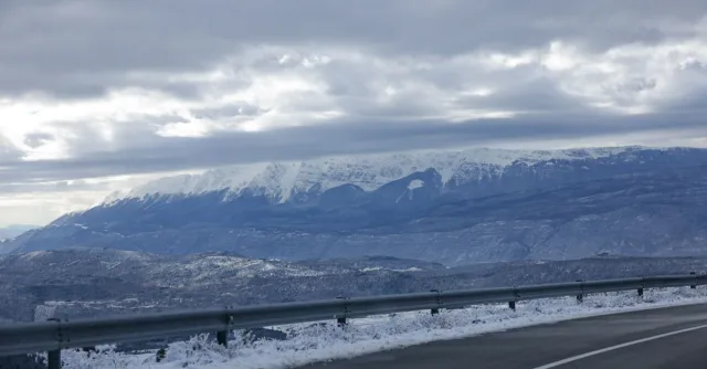 A winding road with snowy mountains under a cloudy sky creates a picturesque winter scene.