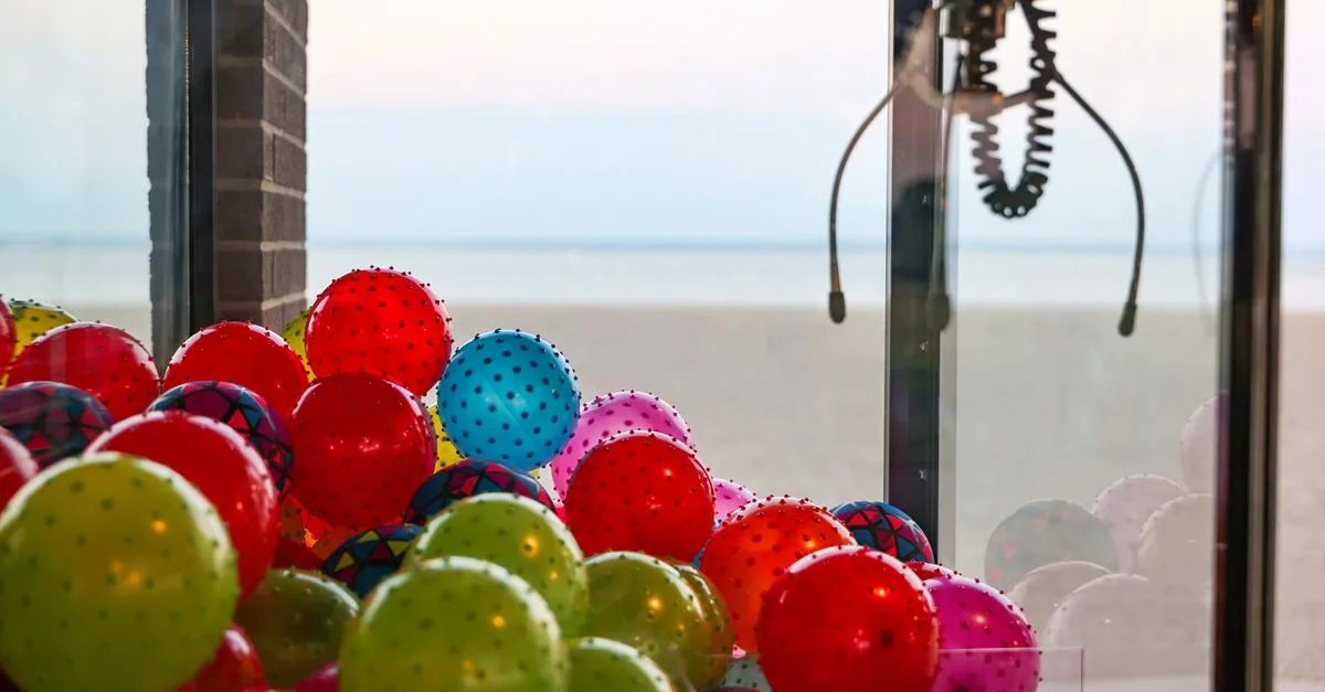 Bright claw machine with colorful balls overlooking the tranquil beach scenery.