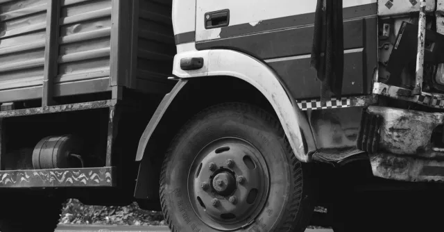 Monochrome close-up of a rugged industrial truck wheel and body detail.
