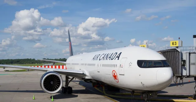 Air Canada Boeing 777 airplane parked at an airport gate under a clear blue sky.