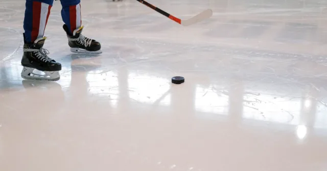 Dynamic shot of a hockey player maneuvering with stick and puck on ice rink.
