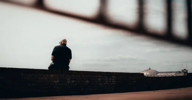 A solitary man sits contemplatively on a wall in Brighton and Hove, England.
