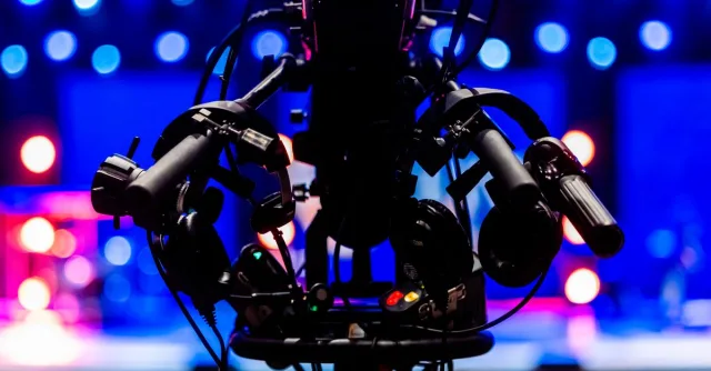 Silhouette of a professional video camera with colorful stage lights in the background.