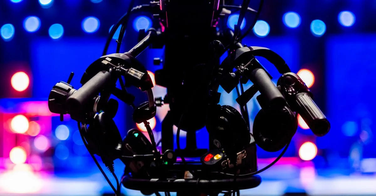 Silhouette of a professional video camera with colorful stage lights in the background.