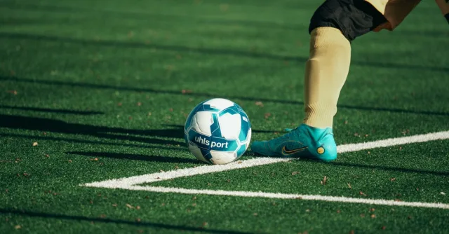 Close-up of a football player preparing to kick a blue and white soccer ball on a turf field.