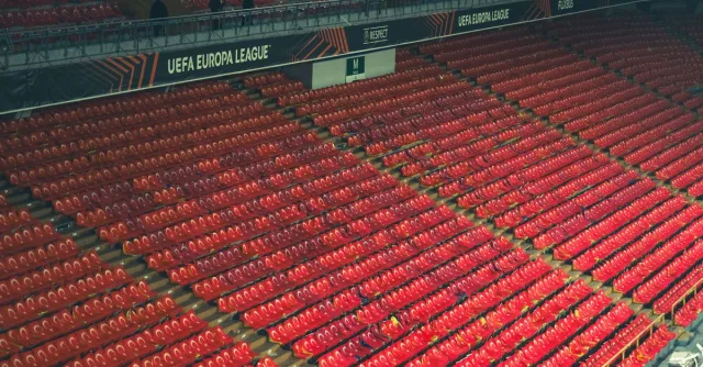 Empty red stadium seats at UEFA Europa League venue, providing spacious copyspace.