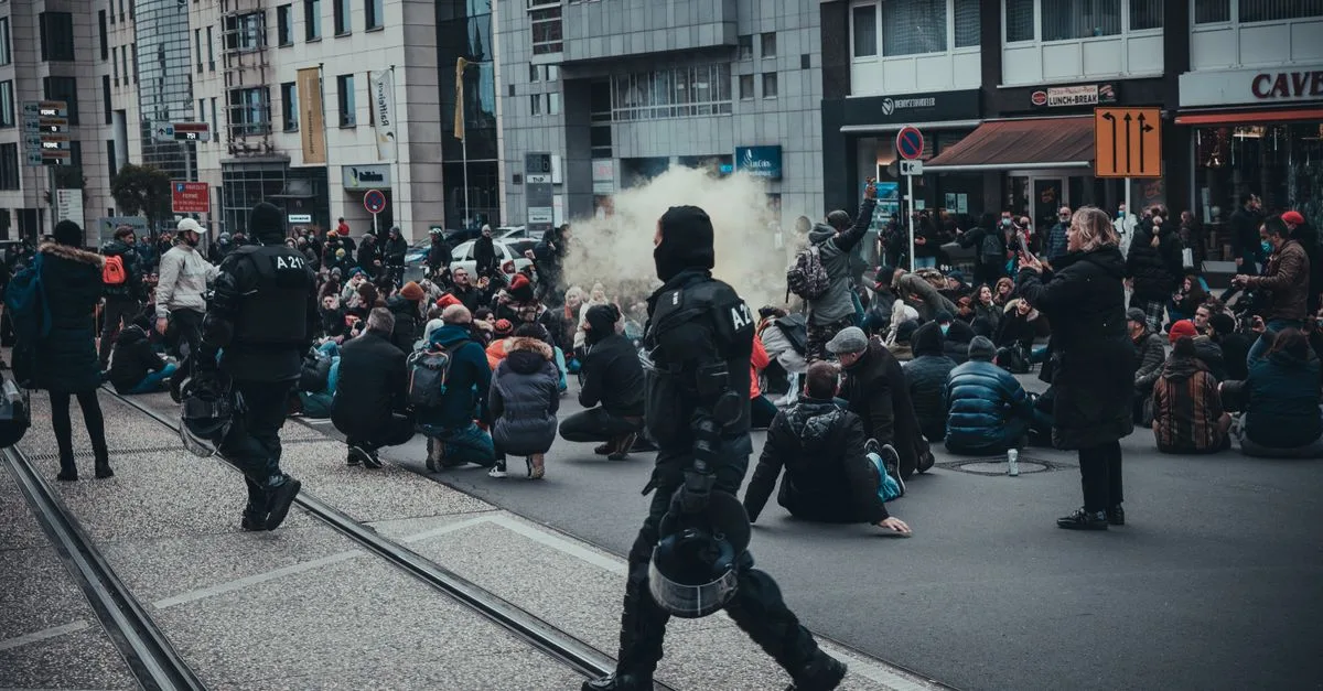 Urban demonstration in Luxembourg City with police and seated protesters, creating a tense atmosphere.