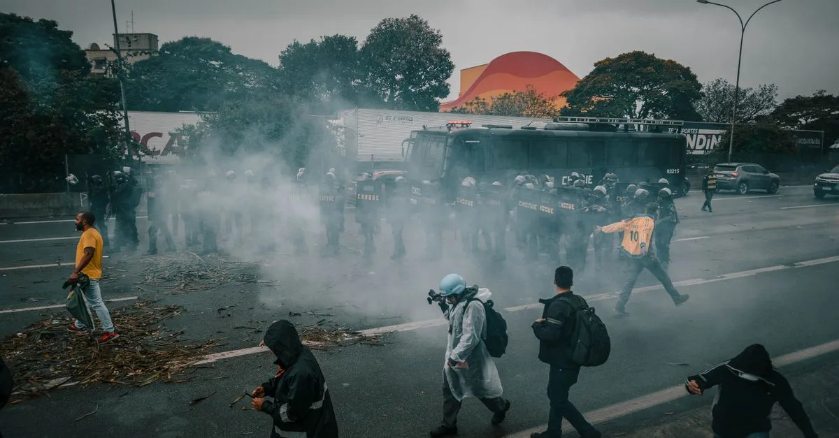 A tense urban protest scene with police and smoke surrounding demonstrators on the street.