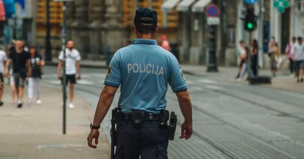 A police officer walking down a city street during the day, maintaining law and order.
