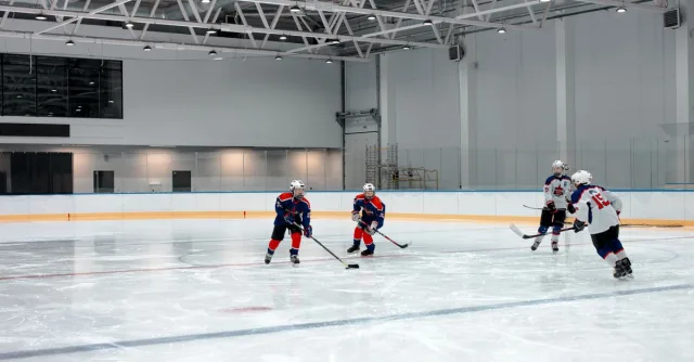Young athletes playing ice hockey in a spacious indoor arena, showcasing teamwork.