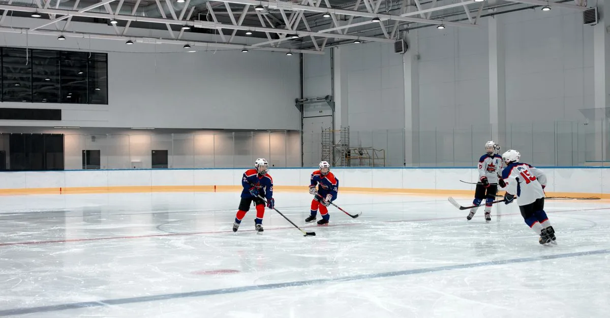 Young athletes playing ice hockey in a spacious indoor arena, showcasing teamwork.