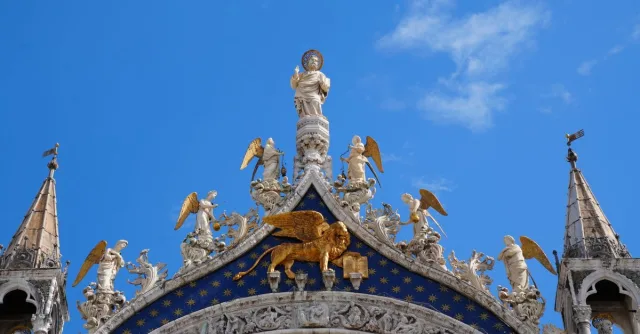 A detailed view of the ornate, angel-adorned facade of St. Mark's Basilica in Venice under a clear blue sky.