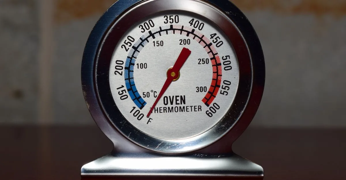 Close-up of a metallic oven thermometer showing temperature in Celsius and Fahrenheit.