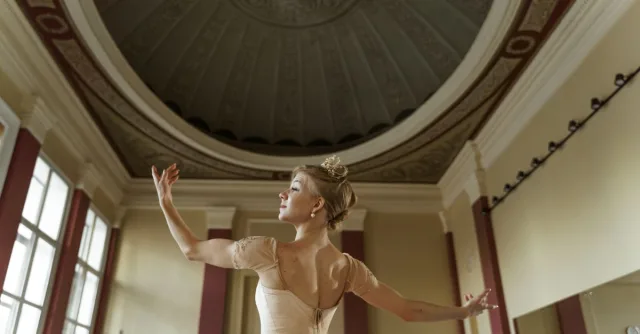 A ballerina elegantly poses in a grand hall, showcasing poise and grace.