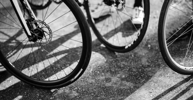Black and white image of multiple bicycle wheels casting shadows on the ground.