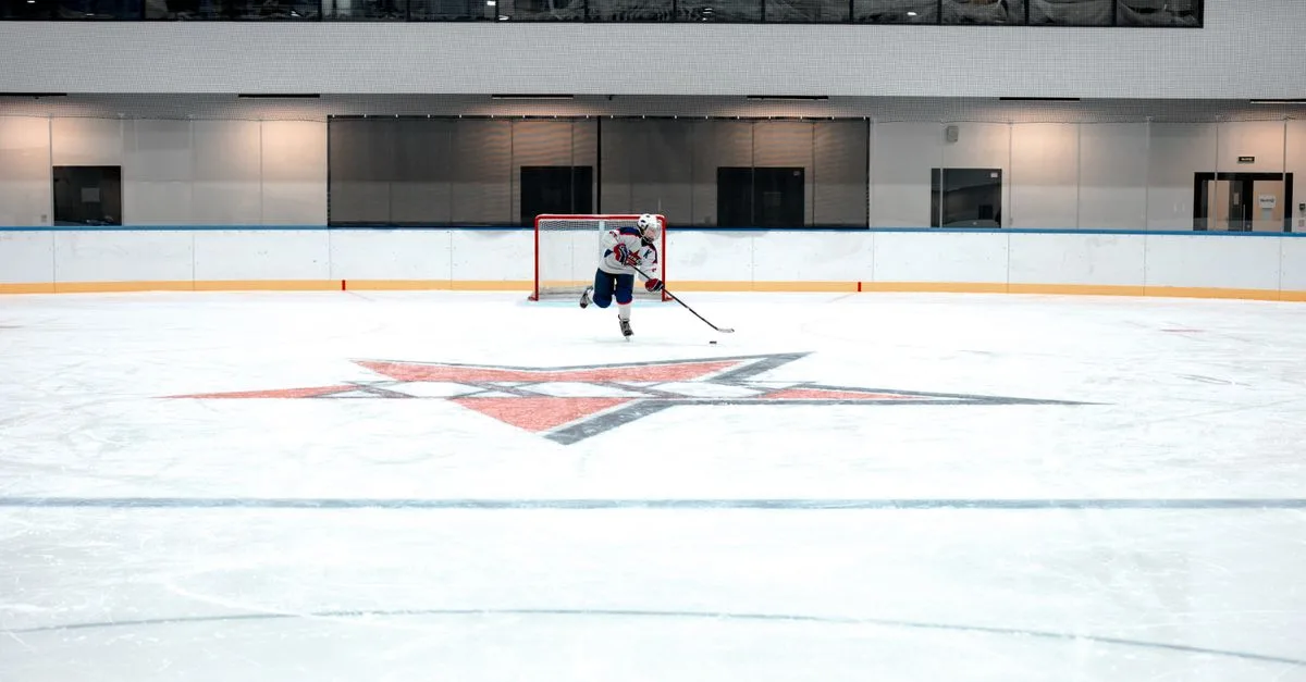 A hockey player in full gear takes a shot on goal in an indoor ice arena.