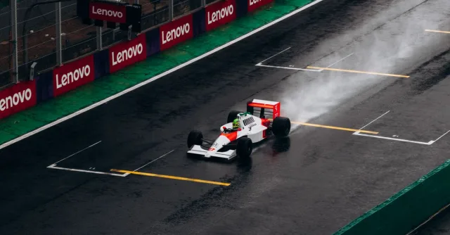 A classic Formula 1 car races on a wet track at Interlagos, Brazil, leaving a trail of spray behind.