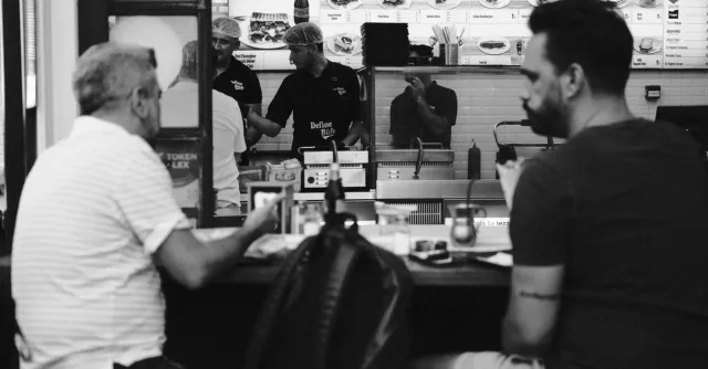 Monochrome photo of a fast food diner with customers and staff behind the counter.