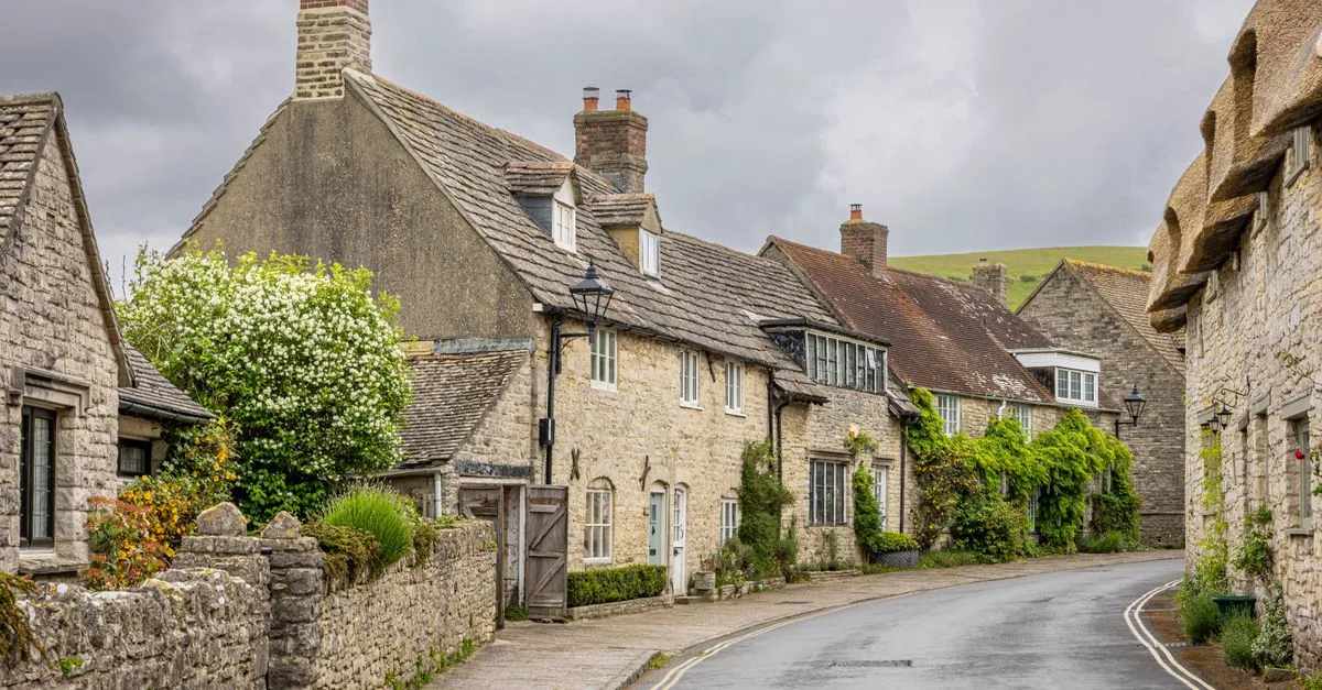 Quaint stone cottages line a quiet road in an idyllic English village setting.