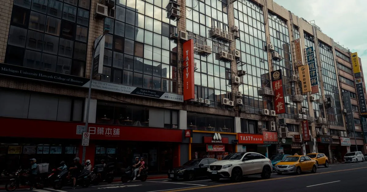 Street view of modern buildings in Taipei with traffic and reflective glass facades.