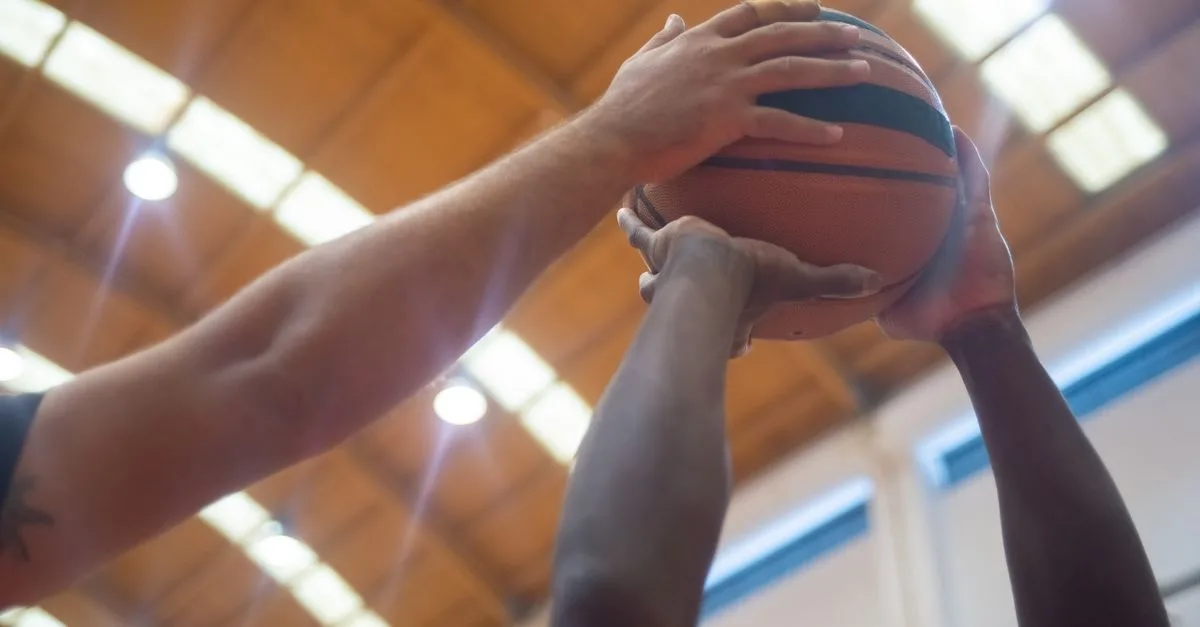 Close-up shot of players competing for the basketball in an indoor court.