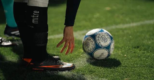 A soccer player in athletic gear prepares for a throw-in during a nighttime match on a grassy field.