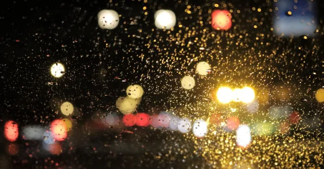 Street lights glistening through raindrops on a car window at night, creating a bright bokeh effect.