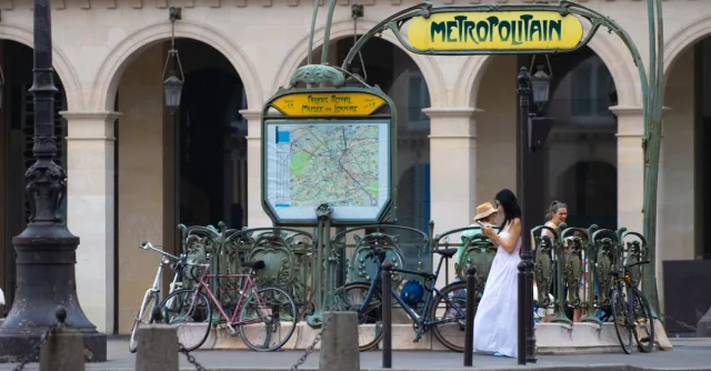 A bustling summer scene at a classic Paris Métro entrance with bicycles and pedestrians.