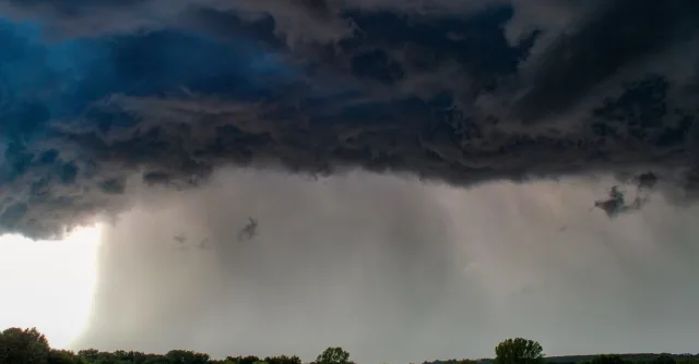 Dark stormy clouds loom over a serene green meadow, signaling an approaching storm.