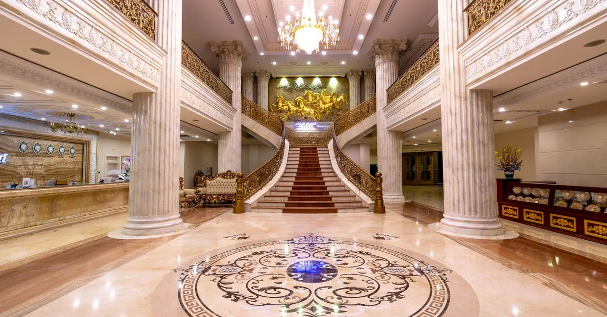 Elegant hotel foyer featuring a grand staircase, marble floors, and a dazzling chandelier.