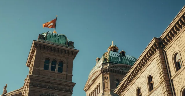 Low-angle view of the Swiss Parliament Building with flag in Berne, Switzerland under a clear blue sky.