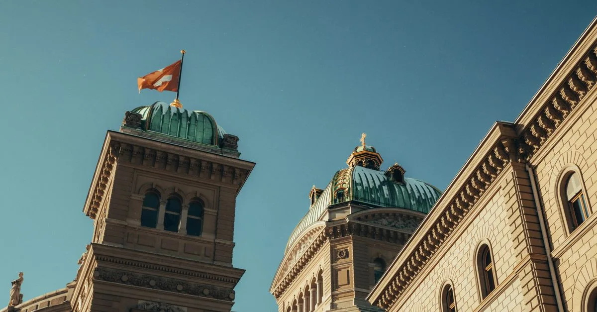 Low-angle view of the Swiss Parliament Building with flag in Berne, Switzerland under a clear blue sky.