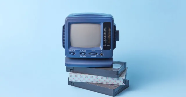 Vintage blue TV set featured atop VHS tapes on a pastel blue background, evoking a retro vibe.