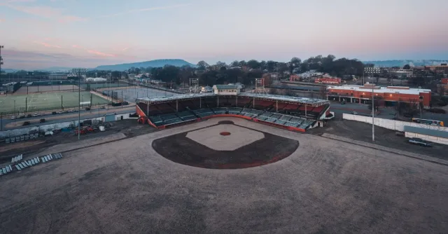 Drone view of empty dry grassy baseball field with tribune near various sports grounds against cloudless sunset sky in town